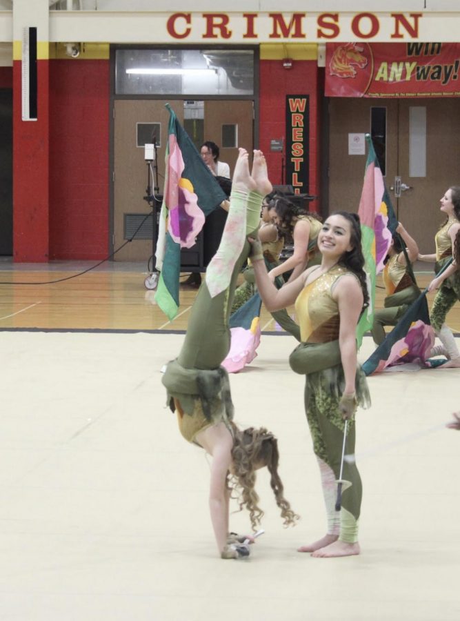 Junior Rebecca Ekema holds a handstand position while Thalia Huys-Hernandez stabilizes her and smiles to the audience in the Elkhart Memorial home showcase in the 2019 winter guard season. 