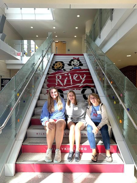 Three pose on a staircase that has the Riley logo on it.